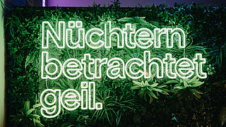 Neon sign reading german text “Nüchtern betrachtet geil.” at the BRANDmania event.