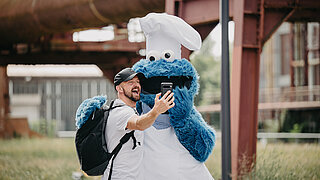 Cookie monster mascot with chef’s hat posing for a selfie with a man.